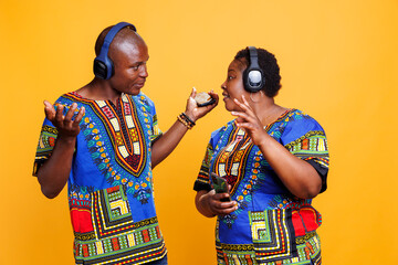 African american couple in wireless headphones listening to music and discussing sound. Man and woman wearing earphones enjoying song and talking while holding smartphone