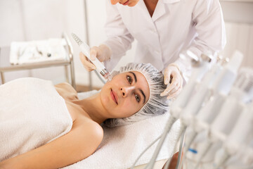 Young female cosmetologist performs cleansing hardware facial procedure on young female patient