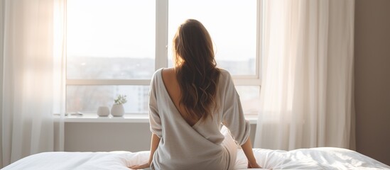 Rear view of young beautiful woman looking at the window after waking up - obrazy, fototapety, plakaty