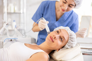 Obraz na płótnie Canvas Young woman receiving facial radiofrequency procedure stimulating collagen production resulting in tightened and firmed skin. Modern hardware cosmetology