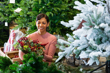 Positive latin american woman who came to the store for shopping chooses a Christmas wreath