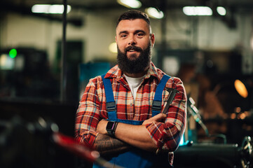 Portrait of a young factory worker, crossed tattooed arms, holding a caliper.