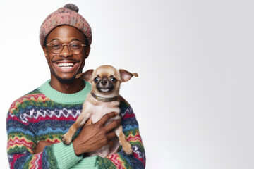 Banner, poster with copy space for International Ugly Sweater Day. African American man in colorful, hilariously terrible sweater and hat, cheerfully laughing, holding adorable Chihuahua puppy dog.