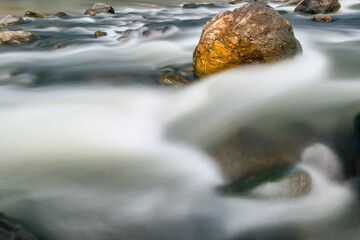 Stone in the midle of the river. Slow motion river water  flows around the stone.