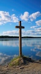 A peaceful scene of a simple wooden cross, p on a tranquil lake shore, reflecting the serene blue of the sky above.