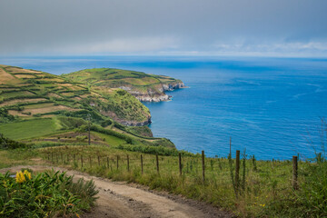 Dirt trail and cliffs seen from Coroa da Mata viewpoint with blue sea in Ribeirinha, São Miguel - Azores PORTUGAL