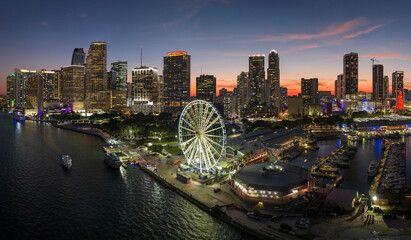 High illuminated skyscrapers of Brickell, city's financial center. Skyviews Miami Observation Wheel at Bayside Marketplace with reflections in Biscayne Bay water and US urban landscape at night - obrazy, fototapety, plakaty