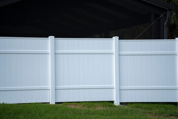 Obraz premium White vinyl picket fence on green lawn surrounding property grounds for backyard protection and privacy