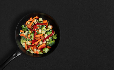 Frying pan with sliced frozen vegetables mix on a black background. Vegetable mix salad. Top view, flat lay. Copy space.
