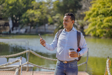 Latino man using a mobile phone on a dock on the shore of a lake.