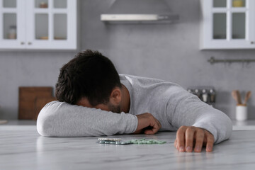 Man with antidepressant pills sleeping at white marble table in kitchen - obrazy, fototapety, plakaty
