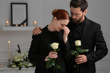 Sad couple with white roses mourning indoors. Funeral ceremony