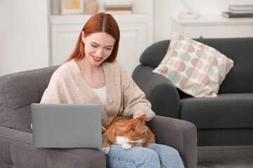 Happy woman with cat working in armchair at home, space for text