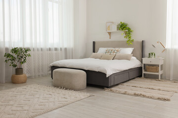 Stylish bedroom interior with large comfortable bed, ottoman and bedside table