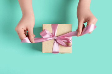 Woman tying bow of gift box on turquoise background, top view - obrazy, fototapety, plakaty