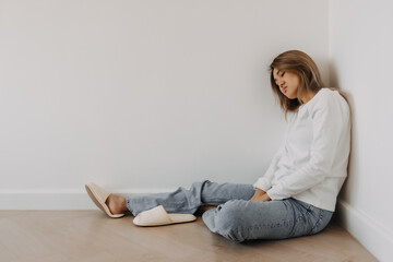 Obraz premium Asian Thai woman sitting on floor and leaning on white wall alone in apartment room. Sick and Tired hopeless and upset disappointed. gloomy depression in winter.