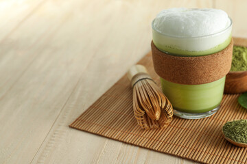 Glass cup of fresh matcha latte, powder and bamboo whisk on wooden table. Space for text