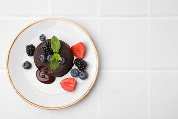 Plate with delicious chocolate fondant, berries and mint on white tiled table, top view. Space for...