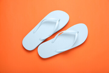 Stylish white flip flops on orange background, top view