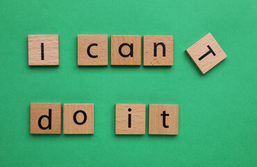 Motivation concept. Changing phrase from I Can't Do It into I Can Do It by removing wooden square with letter T on green background, top view