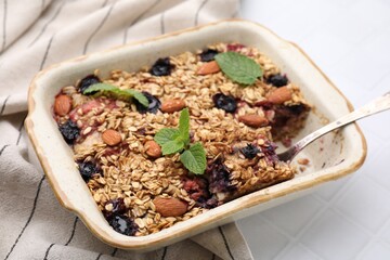 Tasty baked oatmeal with berries and almonds in baking tray on white tiled table, closeup