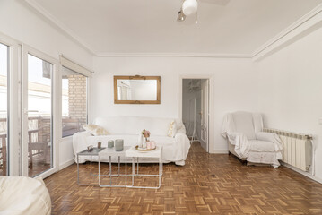 Large living room of an apartment with some white furniture, white lacquered glass access doors, oak parquet floor with checkerboard slats and access to the terrace through white aluminum glass