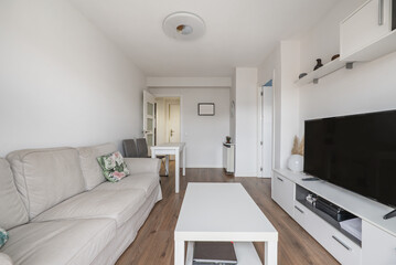 Living room of an apartment with white furniture, a gray fabric sofa and plain white painted walls