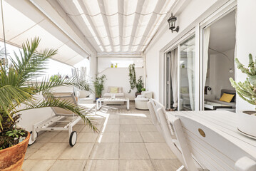 Terrace with white awnings and white wooden furniture in an apartment with white aluminum windows and white painted walls