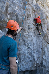 Young man climbing on rock while his colleague holds the safety harness