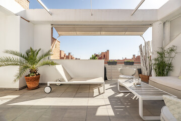 Terrace with white awnings and white wooden furniture combined with a white and gray hammock with wheels, views of the city on a sunny day, some potted plants and gray stoneware floors