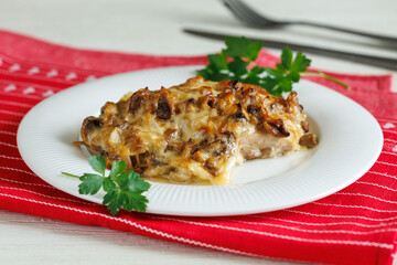 homemade baked chicken fillet steak with mushrooms and cheese on plate on red napkin on white wooden table. Party menu