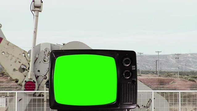Old Television Set Turning On Green Screen with Oil Well Pump Jack in the Background. You can replace green screen with the footage or picture you want with “Keying” effect in After Effects. 4K.