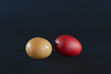 Selective blur on two eggs, one brown egg, one dyed in red, according to the Serbian Easter tradition, isolated on a black background. Painting eggs in red is part of orthodox folklore. © Jerome