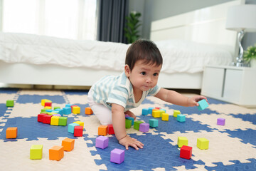 happy infant baby playing wooden block toy on jigsaw mat in bedroom