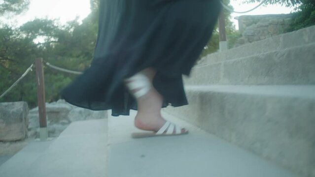 mid shot of person walking up steps in white sandals and dress