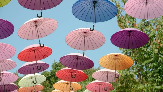 Colorful Umbrellas Hanging Against Blue Sky at Summer Sity Festival - Slow Motion Dolly in Low Angle View. Street Decoration, Celebration, Art, Holiday Alley Decor