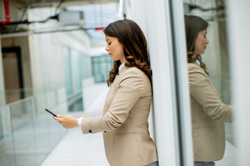Fototapeta premium Young business woman using mobile phone in the office hallway