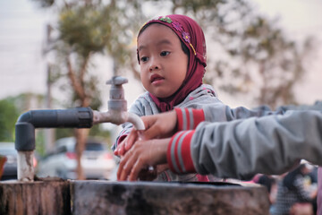 Beautiful female kid learning to wash her hands on a tap water, Yogyakarta 20 September 2023