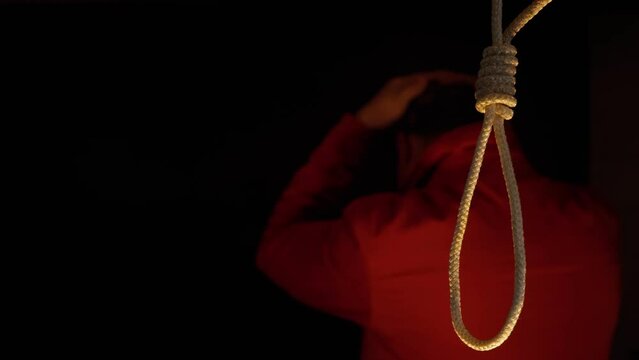 Nervous man against the background of a rope with a suicide noose. Suicide of a person by hanging.