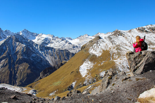 Panoramic picture of a girl sitting on the cliff overlooking mount Elbrus region