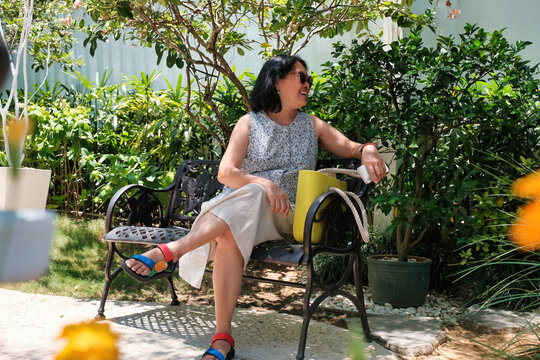 Asian housewife sitting on a park bench in the garden, getting ready to go out