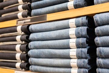 Display shelves with denim pants jeans trousers in department clothes of retail store.
