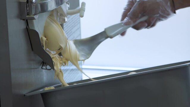 Gelato maker extrudes creamy dessert, hand spoons into metal container