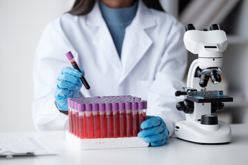 Doctor hand taking a blood sample tube from a rack with machines of analysis in the lab background,...