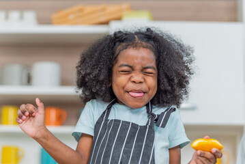 african afro hair black kid sour Acidic taste oranges citrus sour flavour on ripe mouth in kitchen. back african daughter kid afro hair frowning face in taste feelings mood sour Acidic with oranges - obrazy, fototapety, plakaty