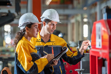 two young engineer assistant in helmet inspection check heavy machine construction installation in industrial metal roof roll sheet factory. colleague friend worker point finger check operation 