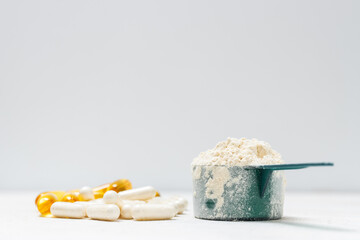 Whey protein powder in measuring spoon, white capsules of amino acids, vitamins and yellow capsules omega 3 on white background, healthy eating and bodybuilding food supplements
