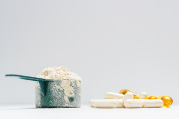 Whey protein powder in measuring spoon, white capsules of amino acids, vitamins and yellow capsules omega 3 on white background, healthy eating and bodybuilding food supplements