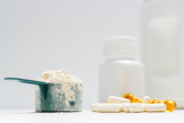 Whey protein powder in measuring spoon, white capsules of amino acids, vitamins and yellow capsules omega 3 on white background, healthy eating and bodybuilding food supplements