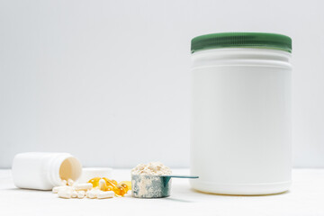 Whey protein powder in measuring spoon, white capsules of amino acids, vitamins and yellow capsules omega 3 on white background, healthy eating and bodybuilding food supplements